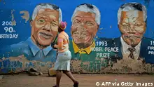 TOPSHOT - Residents walks past murals of late South African former president Nelson Mandela in Soweto, near Johannesburg, on December 7, 2013, two days after his death. The revered icon of the anti-apartheid struggle in South Africa and one of the towering political figures of the 20th century, died in Johannesburg on December 5 at age 95. Mandela, who was elected South Africa's first black president after spending nearly three decades in prison, had been receiving treatment for a lung infection at his Johannesburg home since September, after three months in hospital in a critical state. AFP PHOTO/CARL DE SOUZA (Photo by CARL DE SOUZA / AFP) (Photo by CARL DE SOUZA/AFP via Getty Images)