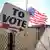 Bandera estadounidense y un letrero en un calle donde pone "A votar".
