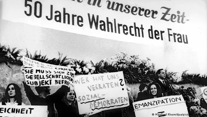 A protest with people holding banners with German slogans, with a large banner marking the 50th anniversary of women's suffrage.