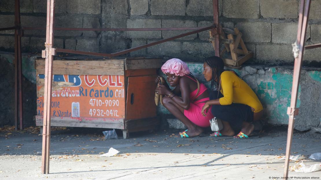 Mujeres se resguardan de las balas durante un enfrentamiento entre policías y miembros de pandillas en la capital de Haití el viernes (01.03.2024).