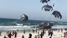 TOPSHOT - This image grab from an AFPTV video shows Palestinians running toward parachutes attached to food parcels, air-dropped from US aircrafts on a beach in the Gaza Strip on March 2, 2024. Israel's top ally the United States said it began air-dropping aid into war-ravaged Gaza on March 2, as the Hamas-ruled territory's health ministry reported more than a dozen child malnutrition deaths. (Photo by AFP)