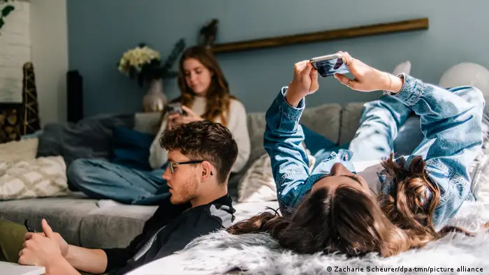 Three teenagers casually sitting on a sofa while surfing the internet with their mobile phones.