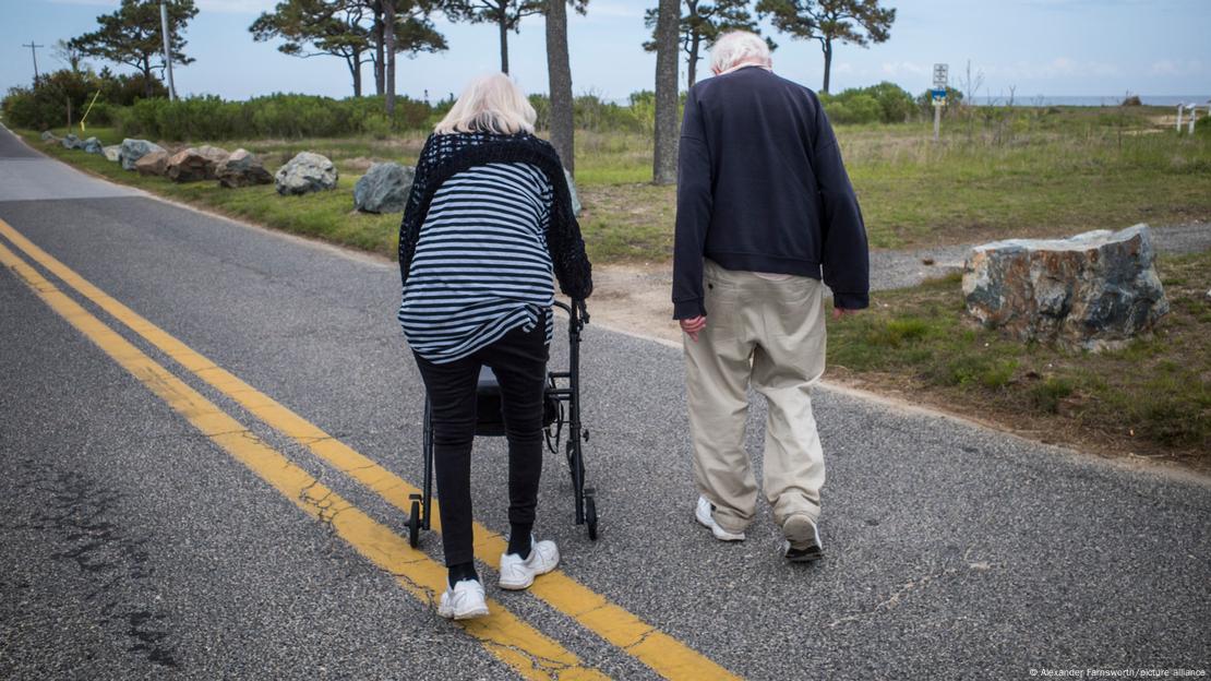 Dos personas mayores, de espaldas, caminan, una de ellas con un andador.