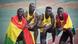 Four men stand smiling. They wear yellow running singlets with the Ghana flag on the front. Two of the men have a Ghanaian flag wrapped around them. Four men stand smiling. They wear yellow running singlets with the Ghana flag on the front. Two of the men have a Ghanaian flag wrapped around them.