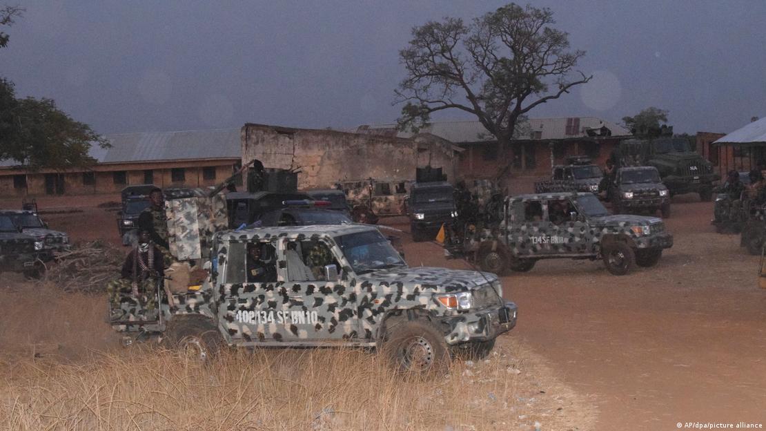 Numeorus Nigeria army trucks are parkd on the sand and dried grass in front of a school in Chikun, Nigeria.