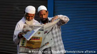 Two elderly men reading a newspaper in India
