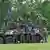 Soldados com roupa militar de camuflagem em frente e em pé sobre um veículo militar blindado