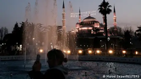 Brightly lit and adorned with religious lettering, the Blue Mosque in Istanbul stands in the twilight. 