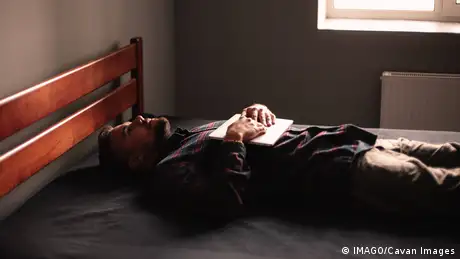 A man lies on a bed with a closed laptop on his chest