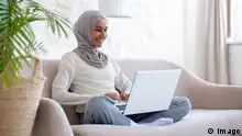 miling young Muslim woman in hijab sitting on couch at home in lotus yoga position and working remotely online on laptop. Model Released Property Released xkwx woman workin