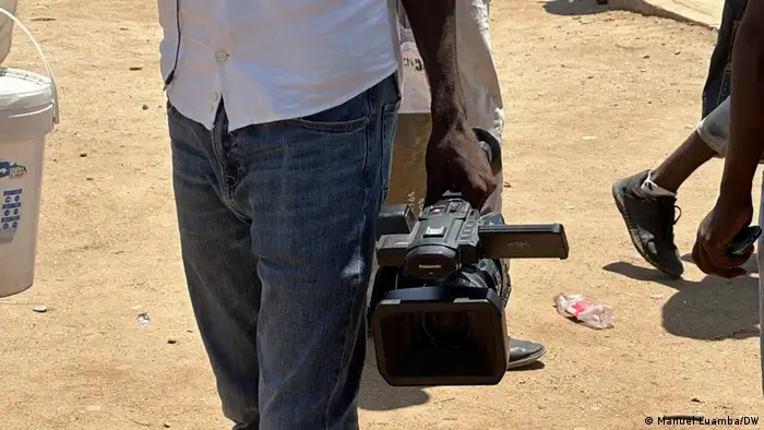 A man in Angola holds a large TV camera in his hand.