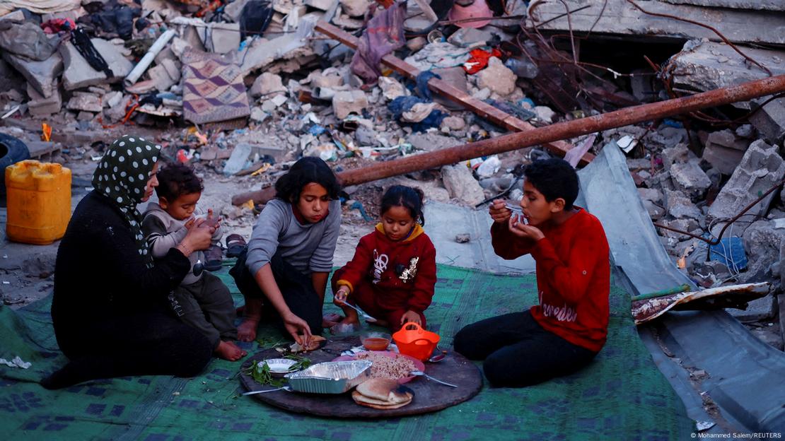 Un mujer y cuatro niños comen sentados en el suelo entre ruinas en Rafah, Franja de Gaza. Un mujer y cuatro niños comen sentados en el suelo entre ruinas en Rafah, Franja de Gaza.