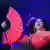 Diana Ross im roten Kleid mit Fächer und Mikrofon auf der Bühne 
