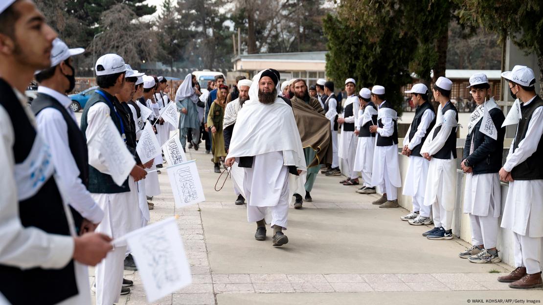Filas de hombres jóvenes en una escuela con banderas talibanas, y un grupo de hombres llegando a un acto académico. Filas de hombres jóvenes en una escuela con banderas talibanas, y un grupo de hombres llegando a un acto académico.