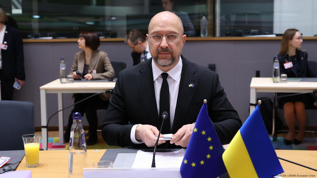 Denys Shmyhal ulur në tavolinë, para tij mikrofoni dhe flamuri ukrainas dhe ai i BE
