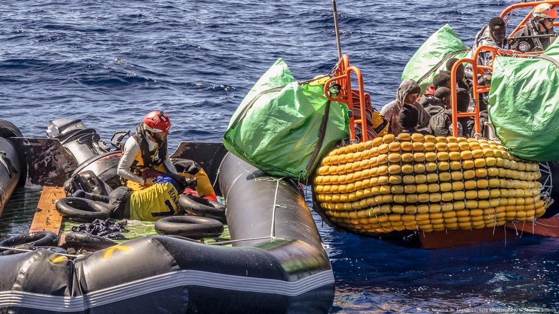 A migrant is helped evacuate a partially deflated rubber dinghy by the rescue personnel