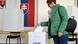 Una mujer deposita su voto en una urna mientras se aprecia una bandera eslovaca en la pared. Una mujer deposita su voto en una urna mientras se aprecia una bandera eslovaca en la pared.