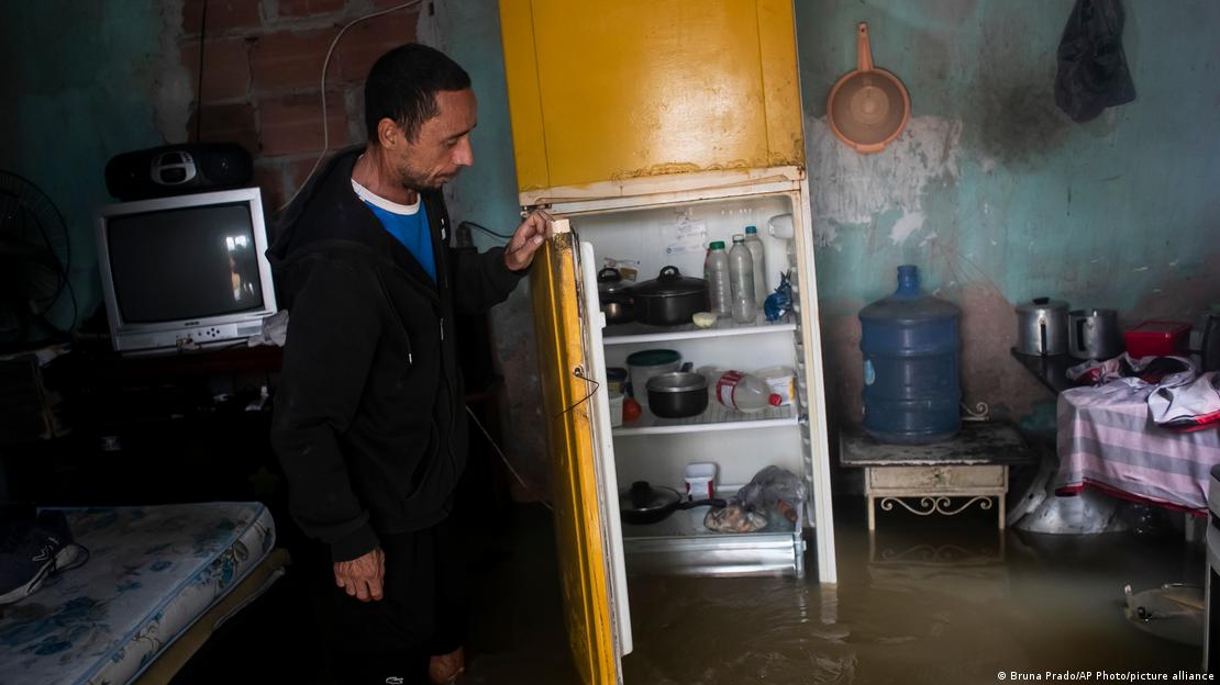 A man, standing in calf-high water, opens the door of a refrigerator as he inspects his flooded home