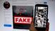 Tela de computador mostra a palavra "fake" sobre uma foto. Em primeiro plano, a foto de um prédio destruído é exibida em um smartphone