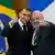 Os presidentes da França, Emmanuel Macron, e do Brasil, Lula, fazem sinal de joinha e sorriem para a câmera durante recepção no Planalto. Ao fundo, vê-se as bandeiras dos dois países