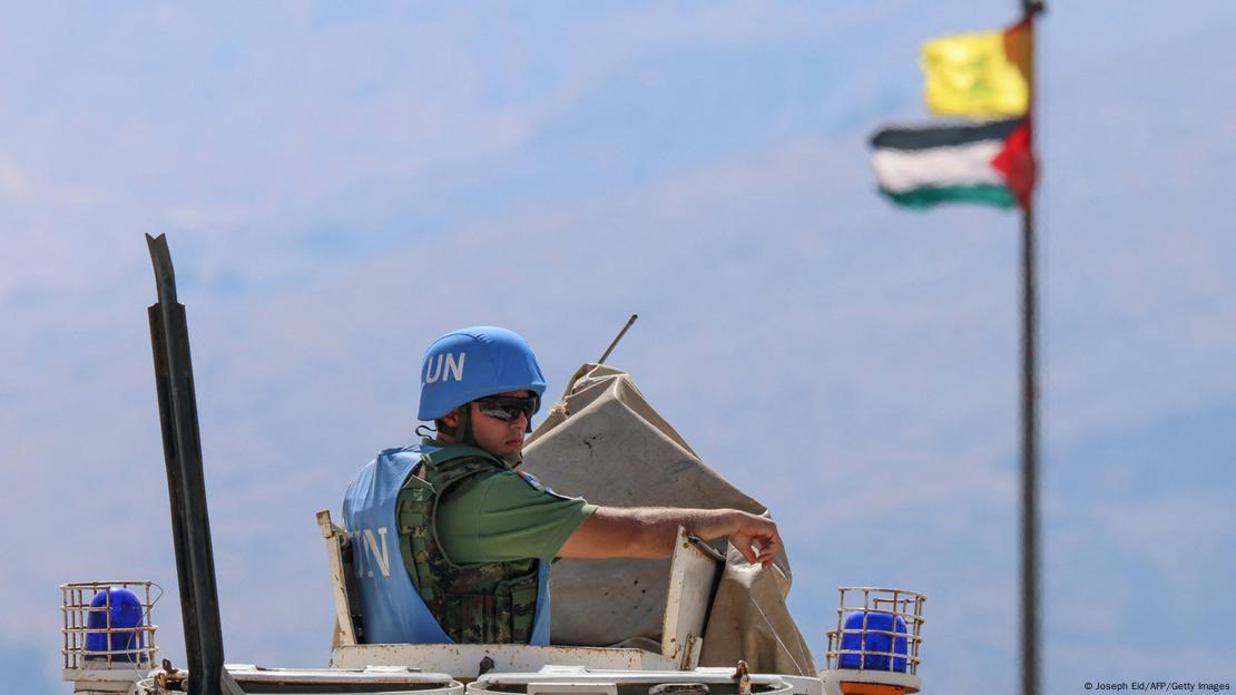 Soldado com capacete azul da ONU sobre tanque, com bandeira palestinense em mastro junto com bandeira do Hezbollah ao fundo