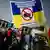 A graphic of a crossed-out military tank is superimposed on the blue and gold Ukrainian flag.