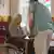 Elderly woman in a wheelchair at a table, with a nurse
