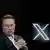Elon Musk is seen beside a large 'X' logo