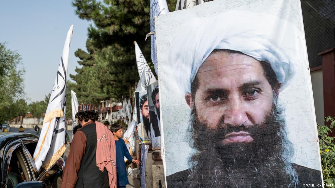 Taliban lideri Hibetullah Ahundzade'nin posterinin yanında bir otomobilin etrafında ellerinde bayraklarla insanlar