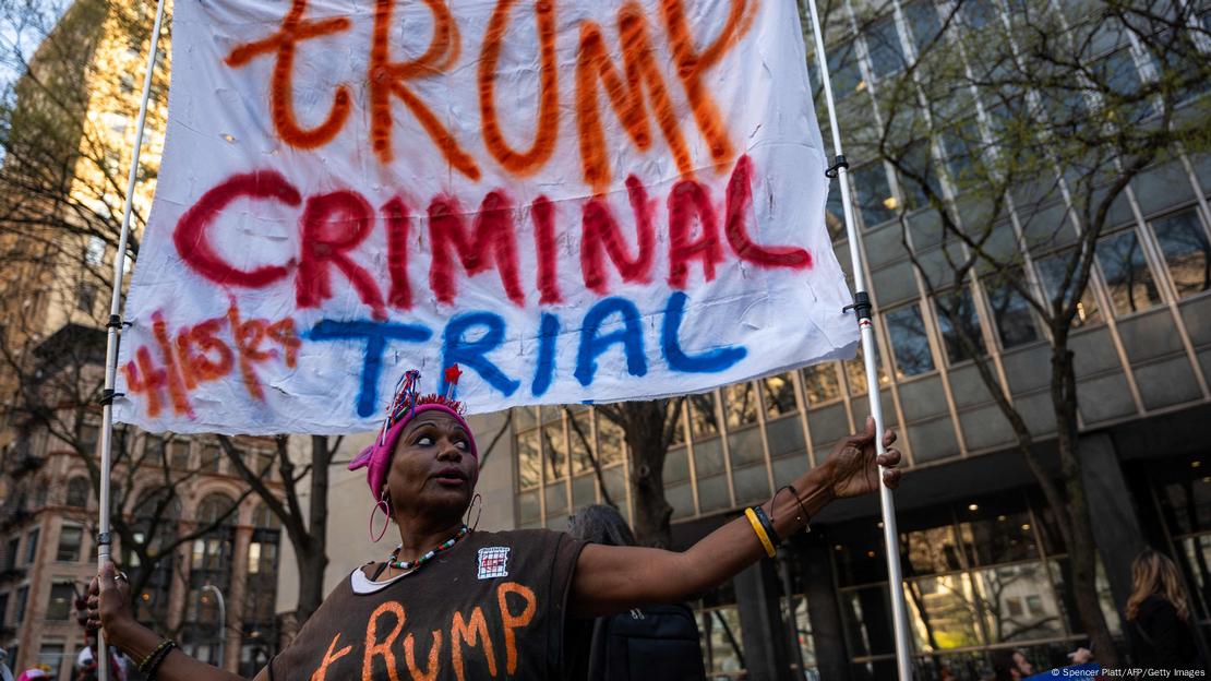 Imagen de una mujer con una pancarta donde se lee "Juicio penal contra Trump".