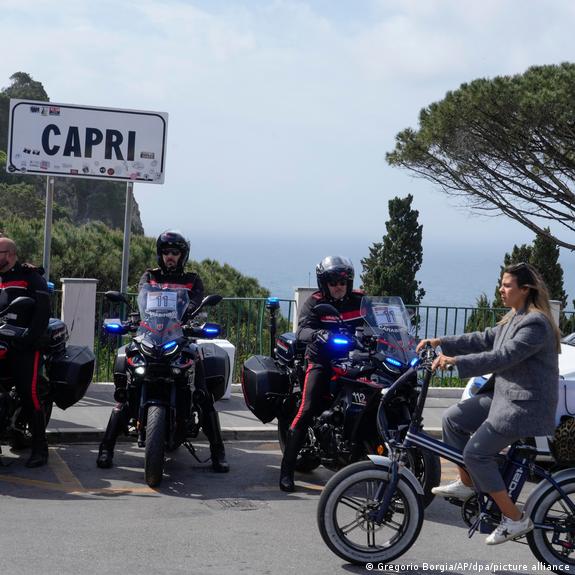 Η αστυνομία κάθεται σε μοτοσικλέτες κάτω από μια πινακίδα που λέει "Capri" καθώς μια γυναίκα περνάει με ποδήλατο.