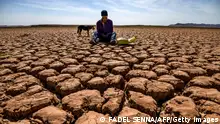 TOPSHOT - A shepherd checks his mobile phones sitting on cracked earth at al-Massira dam in Ouled Essi Masseoud village, some 140 kilometres (85 miles) south of Casablanca, on March 6, 2024. (Photo by Fadel SENNA / AFP) (Photo by FADEL SENNA/AFP via Getty Images)