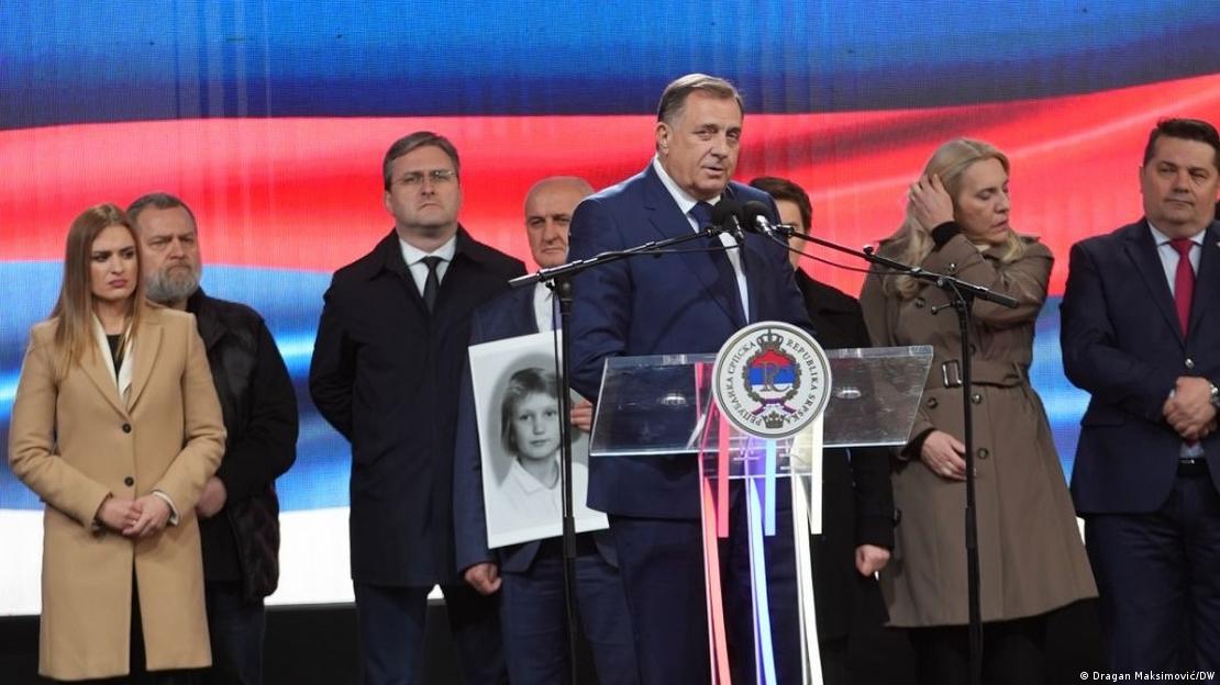 Ein Mann (Milorad Dodik) hinter einem Rednerpult mit Mikrofonen, hinter ihm mehrere Frauen und Männer
