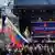 Eine Bühne mit Menschen davor, eine russische Fahne mit dem Bild Wladimir Putins wird geschwenkt