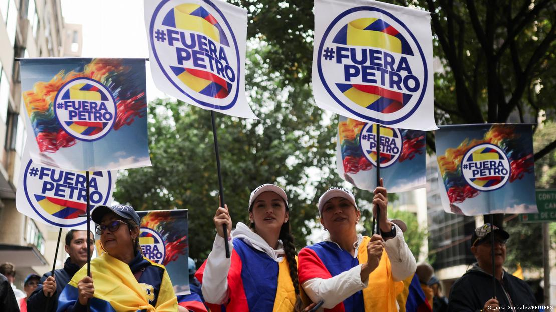 Manifestantes marchan envueltas en la bandera colombiana y sosteniendo carteles en los que se lee "Fuera Petro".