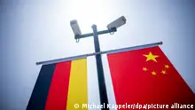 Bandeiras da Alemanha e da China por baixo de câmaras de vigilância