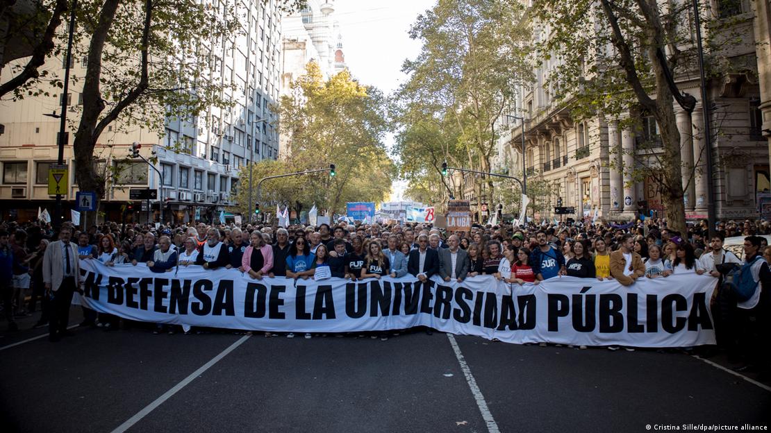 A group of people walk through the streets behind a banner that reads in Spanish "IN defense of public universities" 
