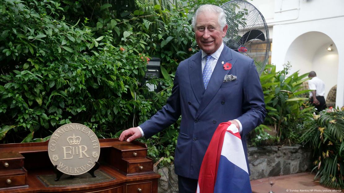 König Charles III - hier 2018 als Prinz - im blauen Anzug vor einer Holzbank mit Commonwealth-Plakate vor dem stellvertretenden Hochkommissariat in Lagos