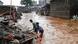 Two men stand in brown swirling floodwaters and sort through items on a concrete platform that was a house Two men stand in brown swirling floodwaters and sort through items on a concrete platform that was a house