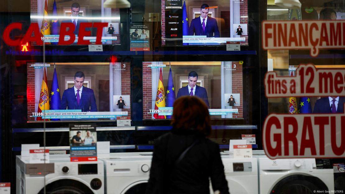 Una mujer observa la comparecencia del presidente del Gobierno español desde el escaparate de una tienda de electrodomésticos de Barcelona.