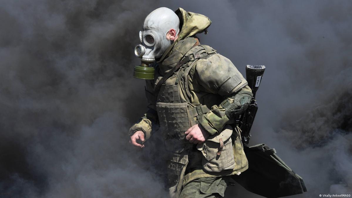 Ein russischer Soldat ist mit Gasmaske und Kampfmontur vor rauchigem Hintergrund zu sehen