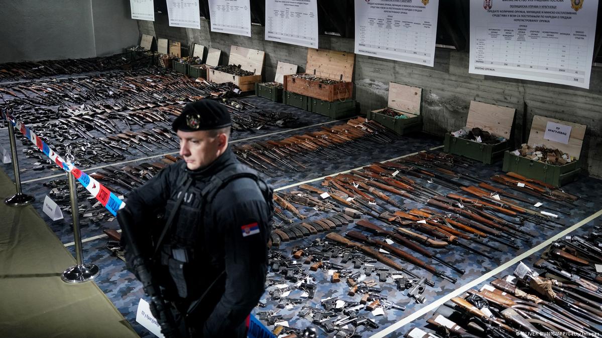In einer Halle liegen zahllose ausgestellte Waffen am Boden, ein Polizist steht davor