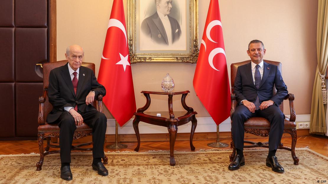 MHP Genel Başkanı Devlet Bahçeli ile CHP Genel Başkanı Özgür Özel yan yana oturuyor, arka planda Türk bayrağı, Atatürk görseli ve MHP bayrağı