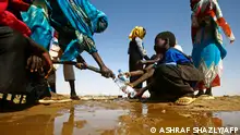 A Sudanese woman fills water bottles held by a young boy about 60 kilometres north of El-Fasher, the capital of the North Darfur state, on February 9, 2017. (Photo by ASHRAF SHAZLY / AFP)