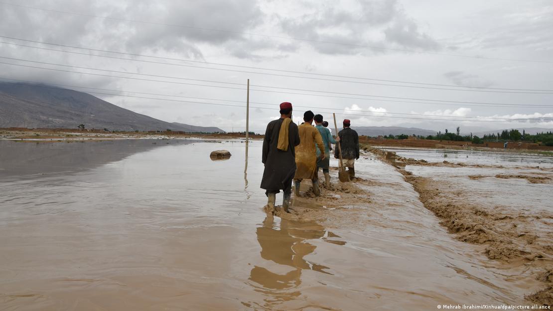 Grupo humano caminha por zona inundada de lama