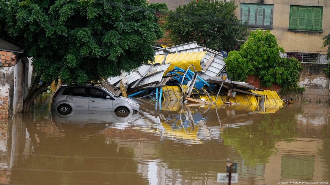 Carro em meio a algamento. Ao fundo, estrutura destruída