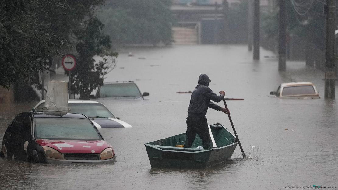 Ein Mann rudert auf einem Boot über eine überflutete Straße an mehreren Autos vorbei, die fast bis zum Dach im Wasser stehen