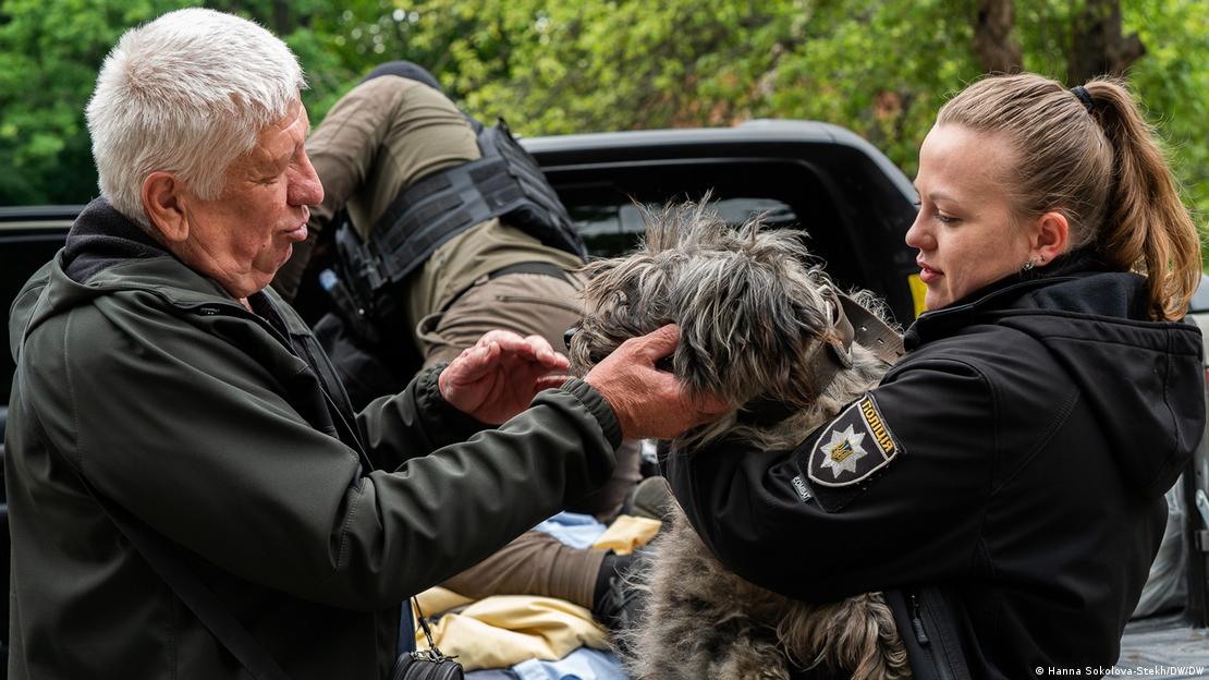 Homem idoso acaricia cachorro peludo no colo de uma mulher policial fardada