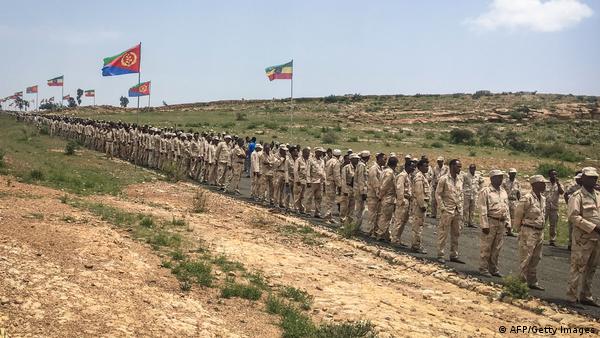 Eritrean soldiers in line, with Eritrean and Ethiopian flags on flagpoles in the backgorund