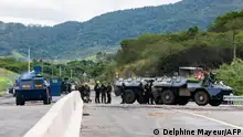 Security officials and armored vehicles of the French Gendarmerie stand guard on the RT1, securing a machine clearing debris and rubbish from the road in the commune of Paita, France's Pacific territory of New Caledonia on May 19, 2024. French forces smashed through about 60 road blocks to clear the way from conflict-stricken New Caledonia's capital to the airport but have still not reopened the route, a top government official said on May 19, 2024. (Photo by Delphine Mayeur / AFP)